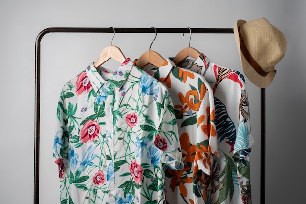 Kostenloses Foto kleiderständer mit hawaiianischen hemden mit blumendruck auf kleiderbügeln und hut