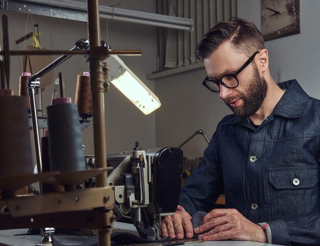 Kleidung herstellen. Schneider sitzt am Tisch und arbeitet an einer Nähmaschine in einer Nähwerkstatt.