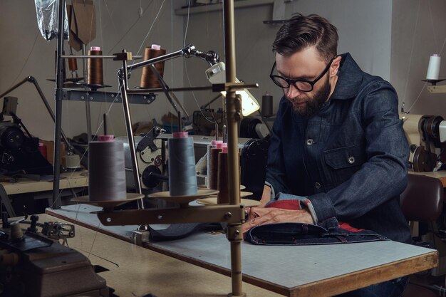 Kleidung herstellen. Schneider sitzt am Tisch und arbeitet an einer Nähmaschine in einer Nähwerkstatt.