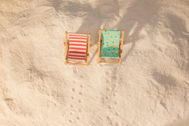 Kleine bunte Liegestühle und Fußabdrücke auf Sand