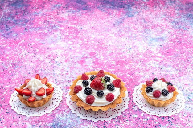 kleine cremige Kuchen mit verschiedenen Beeren auf hellweißem, süßem Kuchen mit Kuchenbeeren