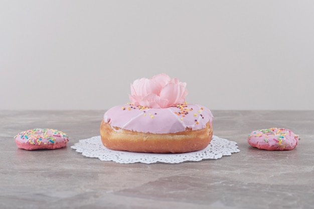 Kleine donuts neben einem großen donut, geschmückt mit einer blume auf marmor