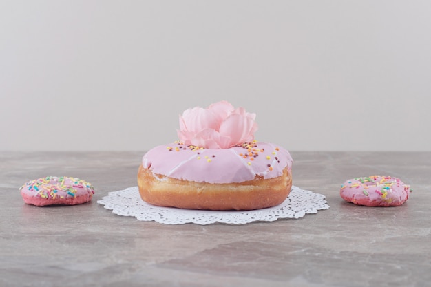 Kleine Donuts neben einem großen Donut, geschmückt mit einer Blume auf Marmor