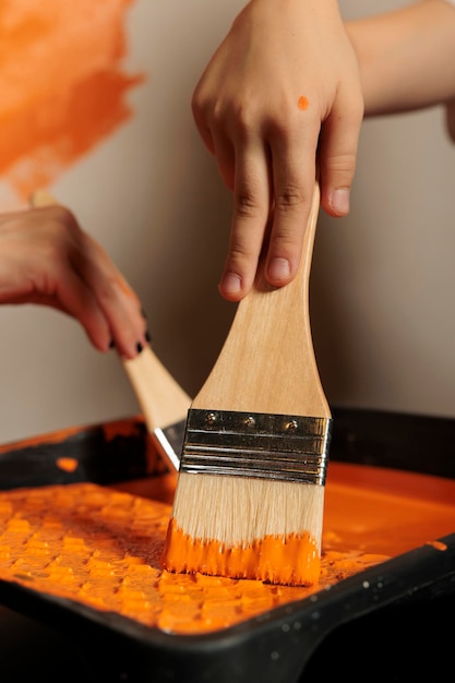 Kostenloses Foto kleine familie, die pinsel und farbe verwendet, um zimmerwände zu streichen, hält pinsel mit borsten in flüssiger acryldose. menschen malen wohnung mit lackierwerkzeugen, erneuerung der oberflächengestaltung. nahansicht.