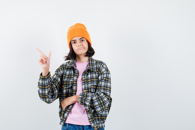 Kleine Frau, die auf die obere linke Ecke in der T-Shirt-Jackenmütze zeigt, die selbstbewusst aussieht