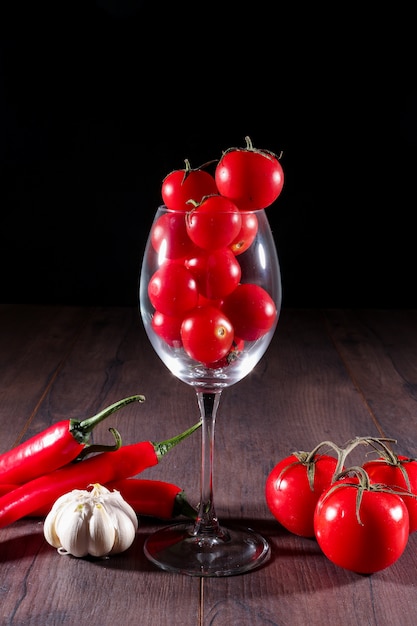 kleine frische Tomaten im Glas auf schwarzem Tisch