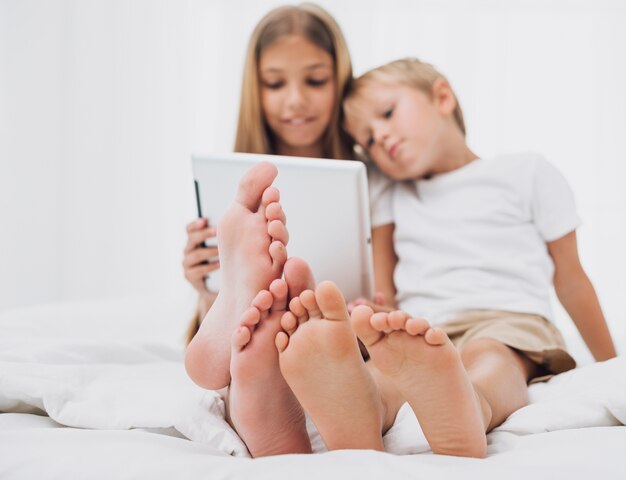 Kleine Geschwister, die im Bett beim Betrachten ihrer Tablette bleiben