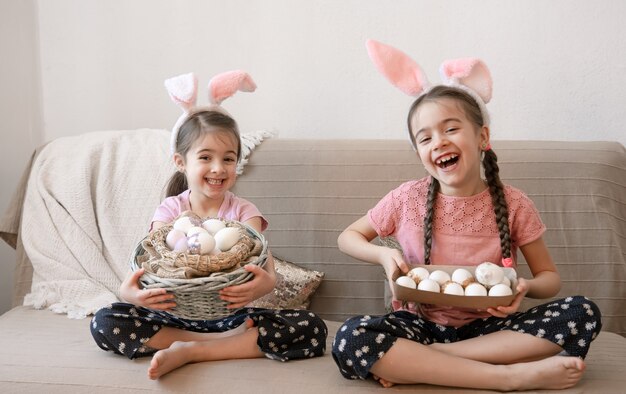 Kleine glückliche Schwestern mit Hasenohren, mit Ostereiern