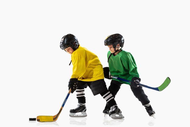 Kleine Hockeyspieler mit den Stöcken auf Eisplatz und weißer Wand. Sportler mit Ausrüstung und Helm üben. Konzept von Sport, gesundem Lebensstil, Bewegung, Bewegung, Aktion.