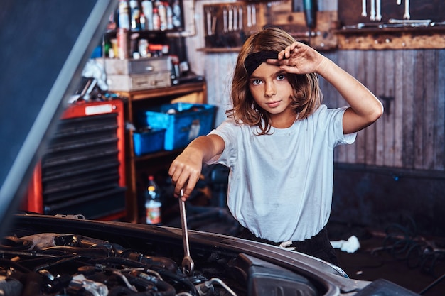 Kleine hübsche Mädchen träumen davon, bei der Autotechnik zu sein, sie versucht, ein kaputtes Auto zu reparieren.