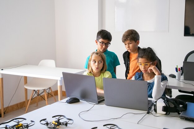 Kleine Klassenkameraden erledigen Gruppenaufgaben, benutzen Laptops und lernen an der Computerschule