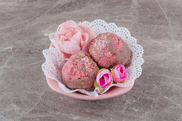 Kleine Kuchen und Blütenkrone in einer mit Deckchen bedeckten Schüssel auf Marmor