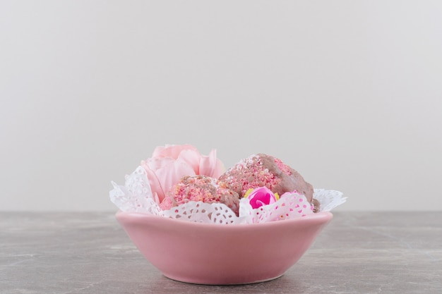 Kleine Kuchen und Blütenkrone in einer mit Deckchen bedeckten Schüssel auf Marmor