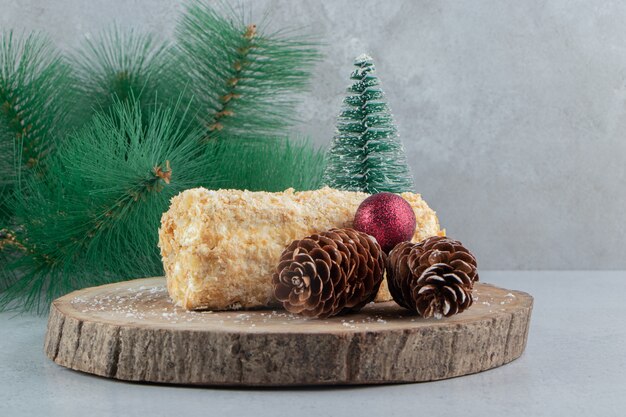 kleine Kuchenrolle neben Weihnachtsschmuck auf einem Holzbrett auf Marmorhintergrund.