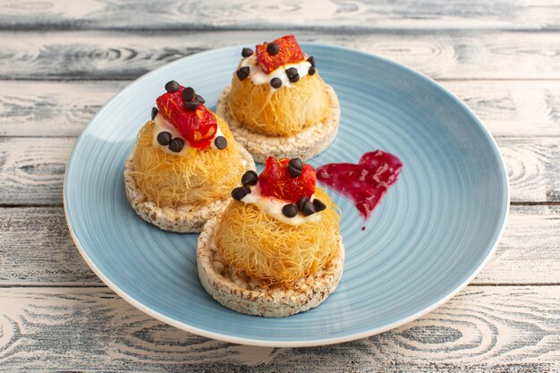 kleine leckere Kuchen mit Sahnefrüchten und Marmelade oben in der blauen Platte auf grau