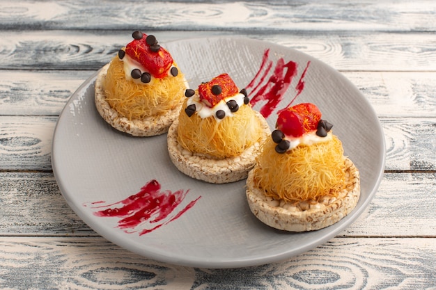 kleine leckere Kuchen mit Sahnefrüchten und Marmelade oben in lila Platte auf grau