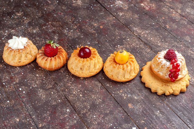 kleine leckere Kuchen und Kekse mit Beeren auf braunem rustikalem Kuchen-Keks-Beeren-Foto-Keks