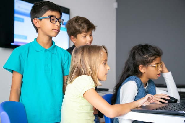 Kleine Mädchen, die Laptops benutzen, an der Computerschule lernen und am Tisch sitzen