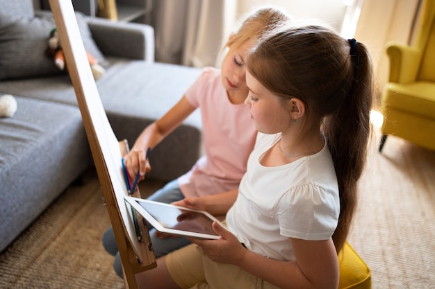 Kostenloses Foto kleine mädchen, die zu hause mit staffelei und tablet zeichnen