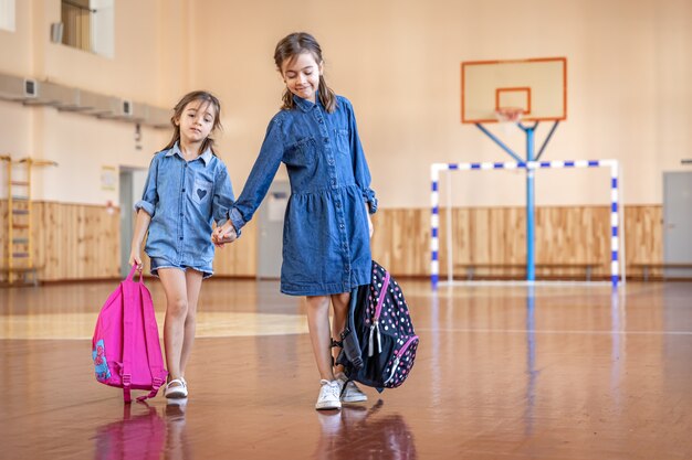 Kleine Mädchen mit Rucksäcken in einer leeren Turnhalle.