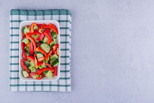 Kleine Platte mit gemischtem Gemüsesalat auf einer erzählten Tischdecke auf Marmorhintergrund. Foto in hoher Qualität