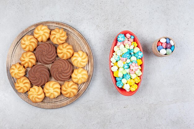 Kleine Schüssel mit Süßigkeiten, große Schüssel mit Popcorn-Süßigkeiten und ein Tablett mit köstlichen Keksen auf Marmorhintergrund. Hochwertiges Foto