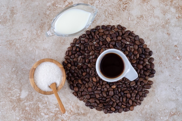 Kleine Schüssel Zucker neben einem Kaffeebohnenhaufen, der eine Tasse Kaffee umgibt