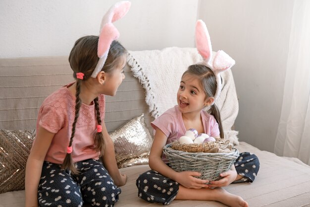 Kleine Schwestern mit Hasenohren, mit Ostereiern zu Hause auf der Couch