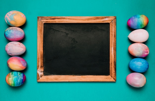 Kostenloses Foto kleine tafel zwischen der reihe von bunten ostereiern auf grünem hintergrund