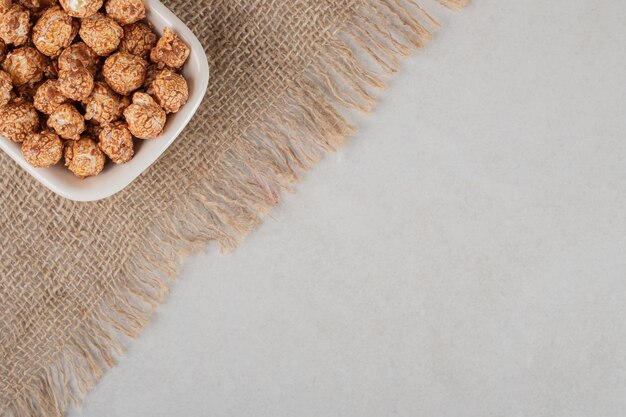 Kleine weiße Schüssel auf einem Stück Stoff gefüllt mit braunem kandiertem Popcorn auf Marmorhintergrund.