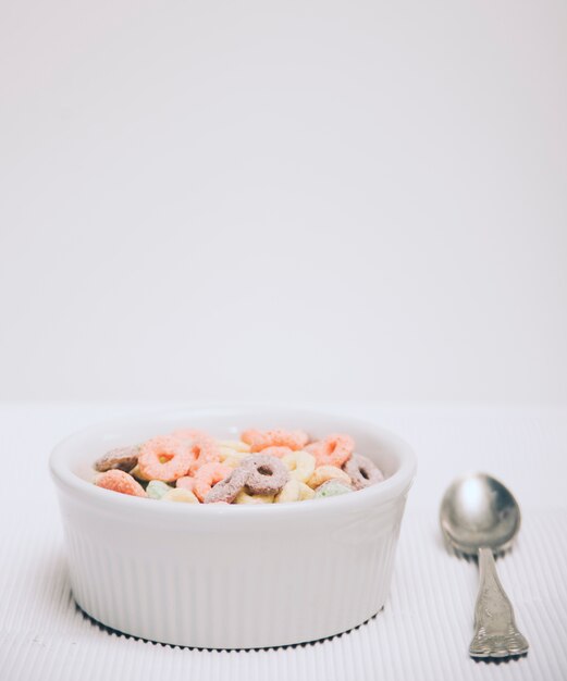 Kleine weiße Schüssel Frühstückskostlöffeln und -löffel gegen weißen Hintergrund