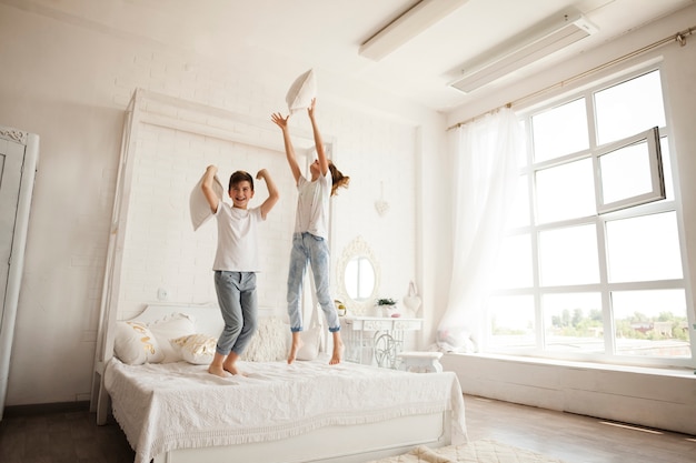 Kleiner Bruder und Schwester, die Spaß beim Springen auf Bett im Schlafzimmer hat