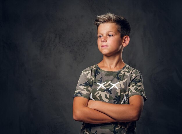 Kleiner charmanter Junge mit schöner Frisur posiert im Fotostudio vor dunklem Hintergrund.