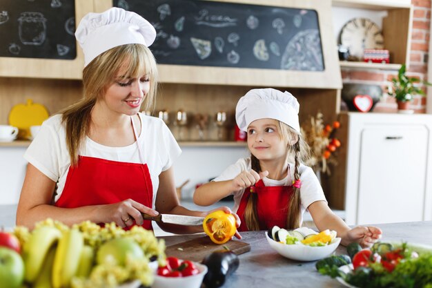 Kleiner Chef Mutter und charmante Tochter bereiten Gemüse in einer gemütlichen Küche zu