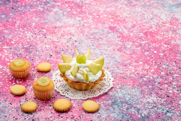 Kostenloses Foto kleiner cremiger kuchen mit geschnittenen fruchtkeksen auf farbigem schreibtisch, kuchen süße zuckerfarbe