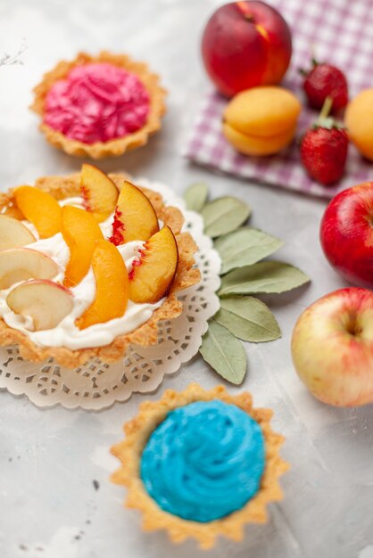kleiner cremiger Kuchen mit geschnittenen Früchten und weißer Sahne zusammen mit cremigen Kuchen und Früchten auf hellem Schreibtisch, Obstkuchen-Kekskeks süß