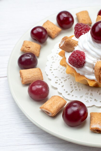 kleiner cremiger Kuchen mit Himbeerkirschen und kleinen Keksen auf weißlichter, süßer Beerencreme mit Obstkuchen