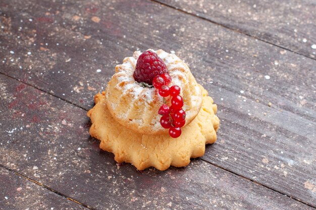 kleiner einfacher Kuchen mit Zuckerpulver Himbeere und Preiselbeeren auf braunem Holz rustikal, Beerenfruchtkuchen süß backen