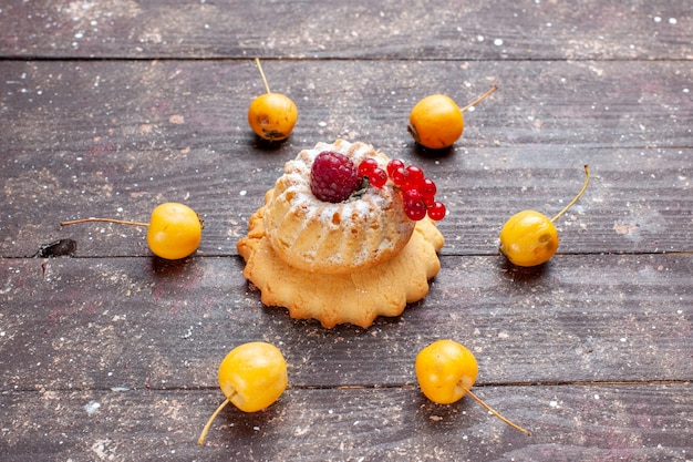 kleiner einfacher Kuchen mit Zuckerpulver Himbeere und Preiselbeeren gelbe Kirschen auf braunem Holz rustikal, Beerenfruchtkuchen süß backen