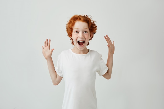 Kleiner hübscher rothaariger junge mit sommersprossen im weißen t-shirt, das super überrascht und glücklich ist