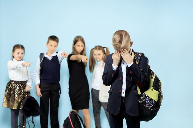 Kleiner Junge, der allein steht und Mobbing erleidet, während Kinder verspotten