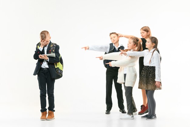 Kleiner Junge, der allein steht und Mobbing erleidet, während Kinder verspotten