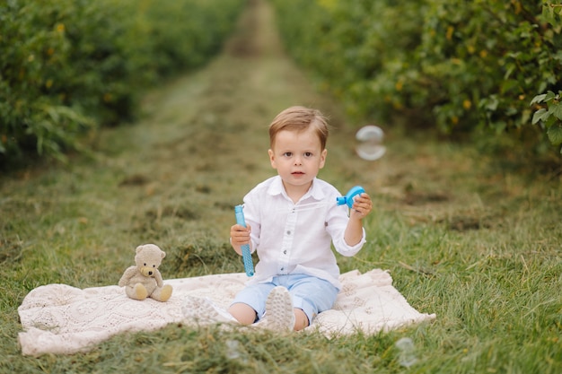 Kleiner Junge, der auf Picknickplaid im Bauerngarten sitzt