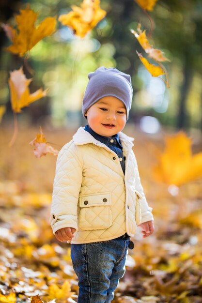 Kleiner Junge, der Blätter im Herbstpark spielt und wirft