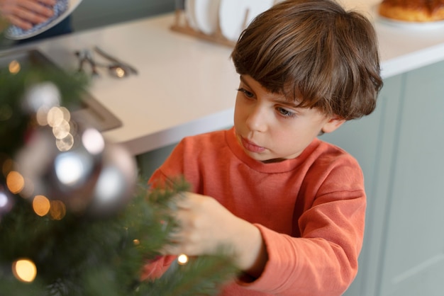 Kostenloses Foto kleiner junge, der den weihnachtsbaum schmückt