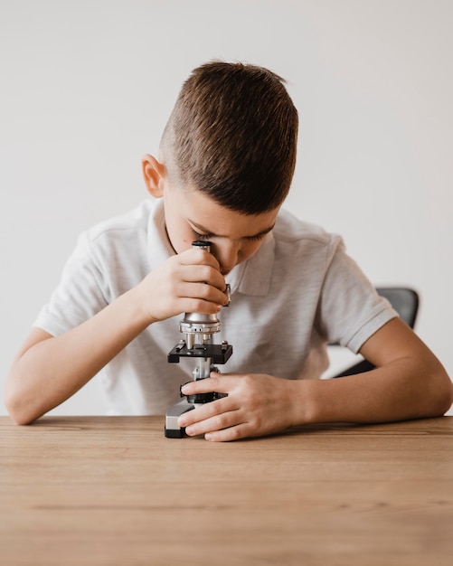 Kleiner Junge, der ein Mikroskop benutzt, um Wissenschaft zu lernen
