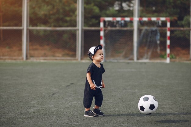 Kleiner Junge, der Fußball in einem Sportplatz spielt