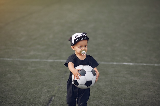 Kleiner Junge, der Fußball in einem Sportplatz spielt