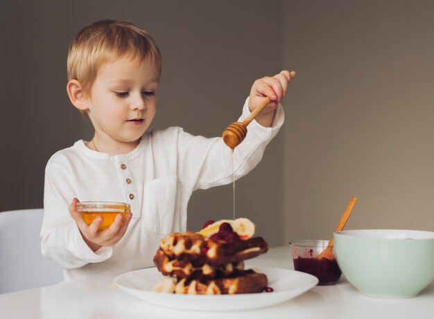 Kleiner Junge, der Honig auf Waffel setzt