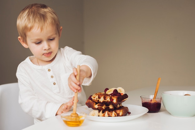 Kleiner Junge, der Honig auf Waffel setzt